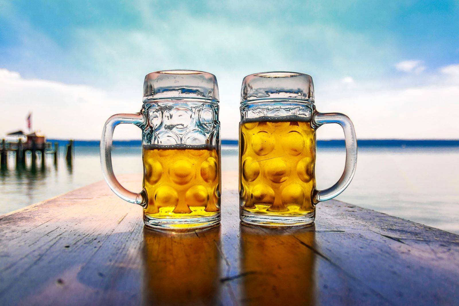 two pints of beer sitting on a table with a beach sunset in the background