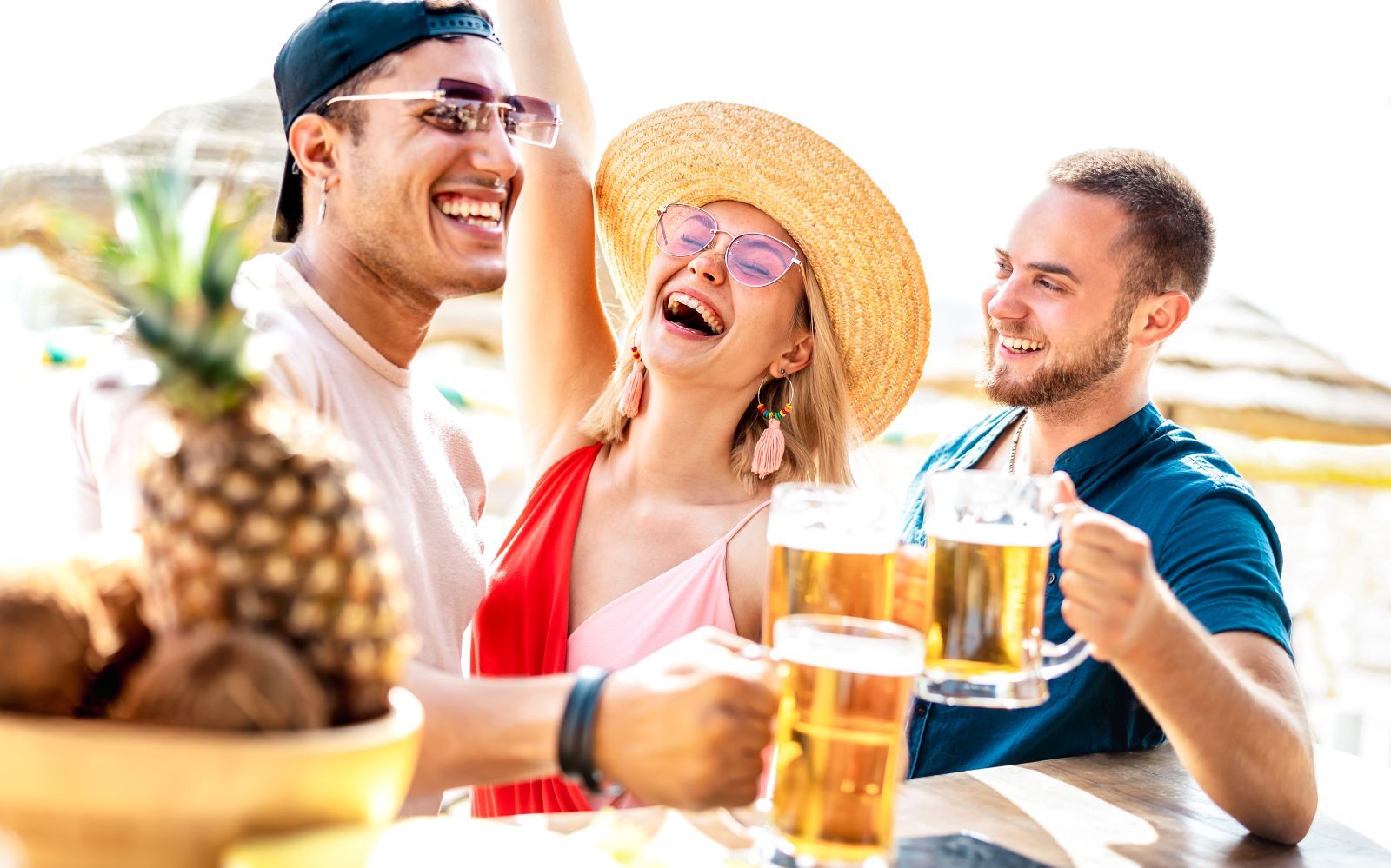 two men and a woman enjoying pints of beer at a beach bar on a sunny day